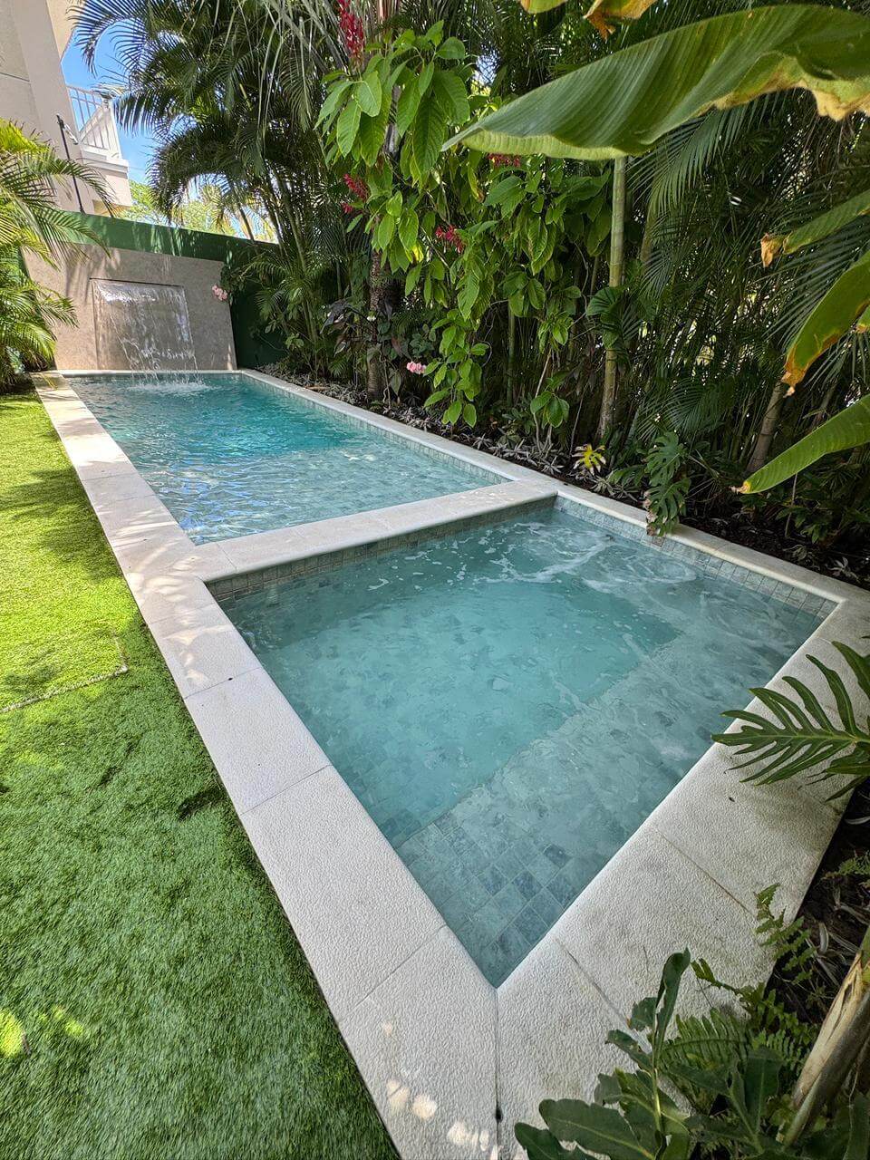 Piscina raia com prainha, cascata em pedra e paisagismo tropical